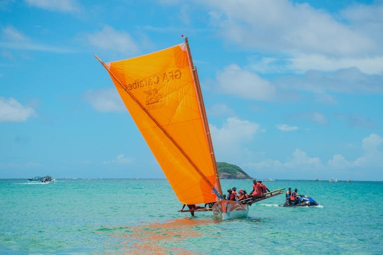 Bright orange sailboat with group enjoying tropical sea adventure under clear blue skies.